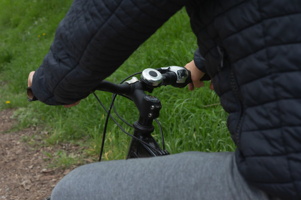 手的特写，十几岁的自行车手握着她的自行车车把，背景是草地图片下载