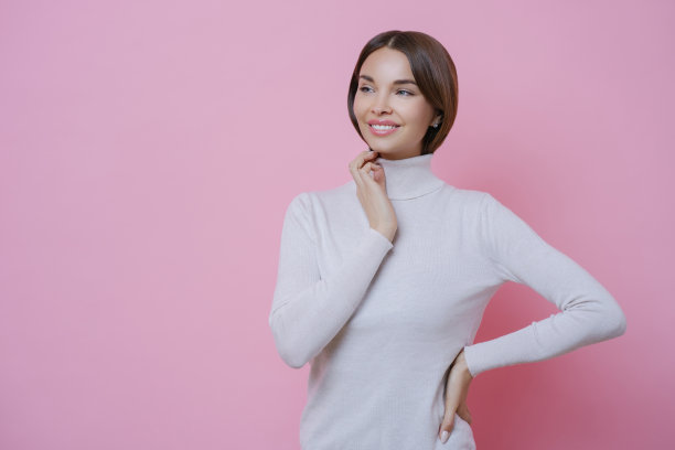 美丽温柔的年轻女子，带着牙齿的微笑，沉思地看着旁边，穿着休闲的白色高领毛衣，心情很好，站在粉红色的背景下，空白的自由空间为你的提升图片下载