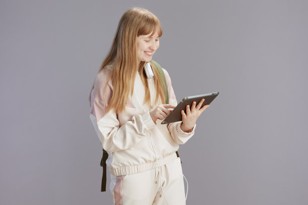 穿着米色运动服，微笑着使用平板电脑的时髦少女图片下载