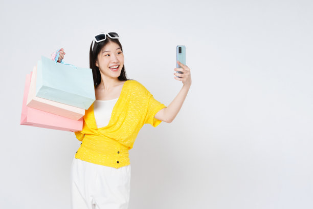 快乐的年轻女子拿着购物袋在白色背景下自拍。图片下载