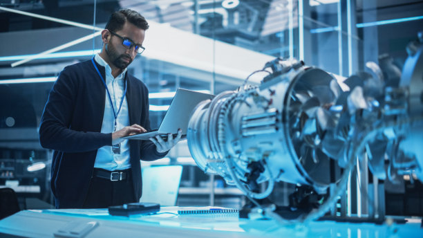 总工程师使用笔记本电脑，分析和研究未来涡轮风扇发动机的工作原理。高级经理开发创新技术在工业高科技设施。图片下载
