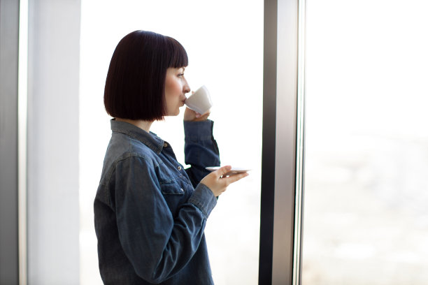 拿着咖啡杯的女人从全景窗口欣赏风景图片下载