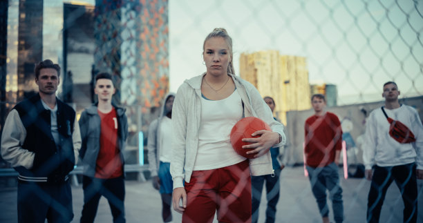 一群不同种族的年轻人站在屋顶上，在城市环境中寻找和摆姿势拍照。镜头聚焦于一个带着红色足球的运动女性图片下载