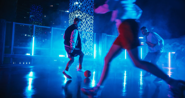 雨后霓虹灯下，多民族的朋友们在屋顶上踢足球。技术娴熟的年轻人带球过人，独自带球过人并得分图片下载