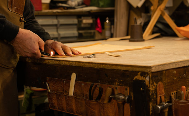 老年皮革工匠在燃烧椅子靠背上多余的线。在他的工作间里，一个旧的工作台上，手工图片下载