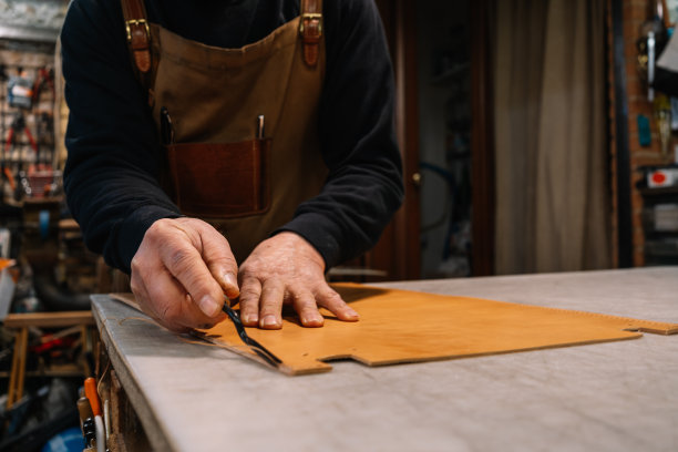 选择性地关注皮革工匠在缝制一块皮革的边缘后绘制多余的皮革图片下载