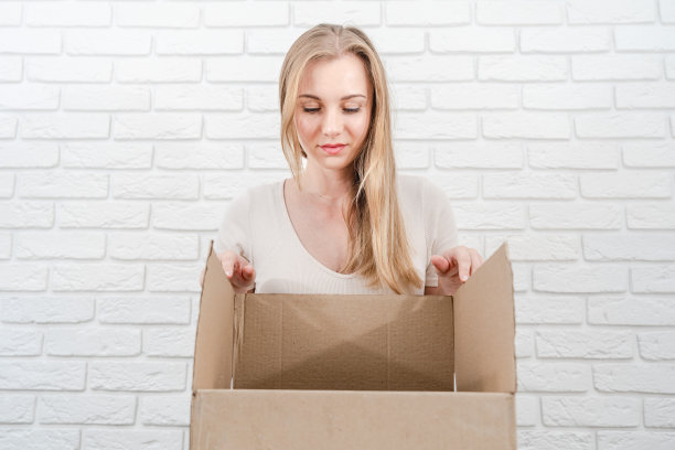 年轻的金发女郎看着一个白砖背景的盒子图片下载