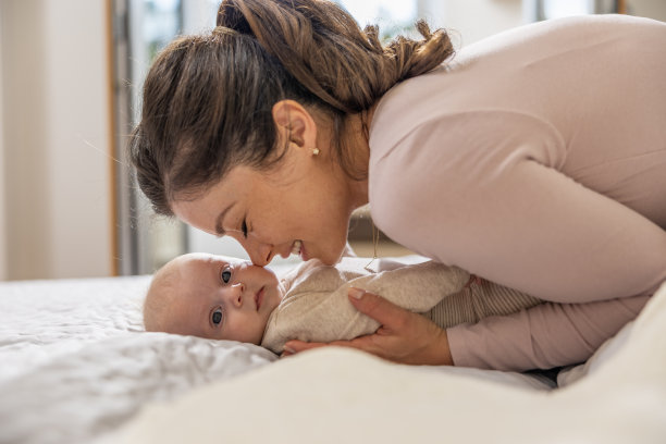 美丽的妈妈和她三个月大的宝宝在卧室里玩耍的照片图片下载