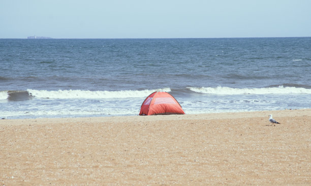 一个橙色的帐篷搭在沙滩上，背景是波涛翻滚的美国弗吉尼亚海滩。图片下载