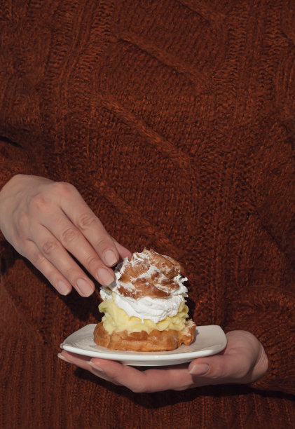 饥饿的小女孩吃着奶油泡芙。最小的食物概念。图片下载