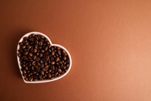 特写:棕色背景上，心形盘子里的烤咖啡豆图片下载