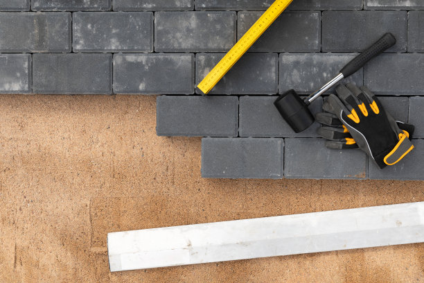 用橡胶锤和手套在沙地上铺设人行道水泥路面的俯视图。房子的改进。图片下载