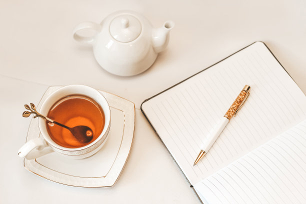 白色的杯子和碟子，金色的勺子、茶壶和记事本图片下载