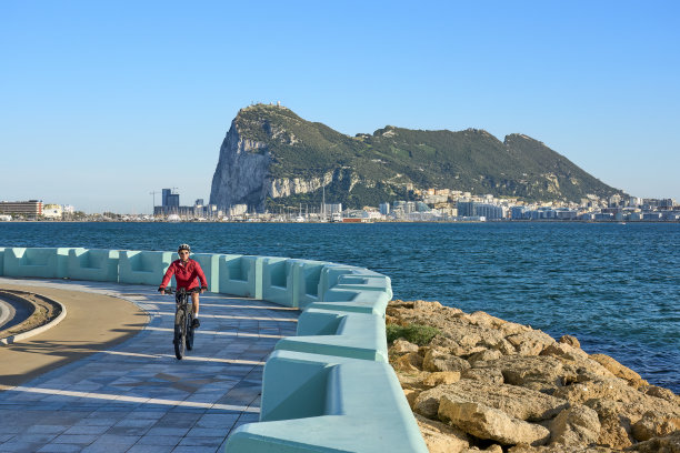 一名女子骑着她的电动山地车在直布罗陀岩石下骑行图片下载