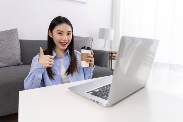 漂亮的年轻女子坐在客厅里，一边用笔记本电脑，一边喝着咖啡图片下载