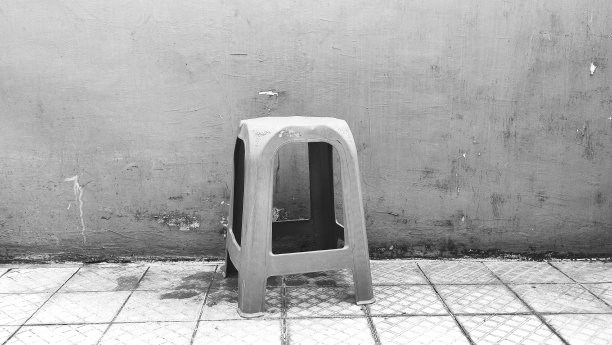一张黑白照片，一张旧塑料椅子对着暗淡的墙壁图片下载