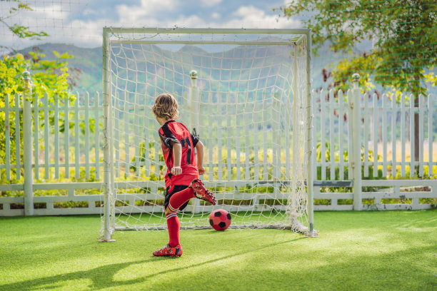 可爱的小男孩穿着红色的足球服踢足球，足球在球场上，在户外。活跃的孩子与孩子或父亲一起运动，微笑的快乐男孩在夏天玩得开心图片下载