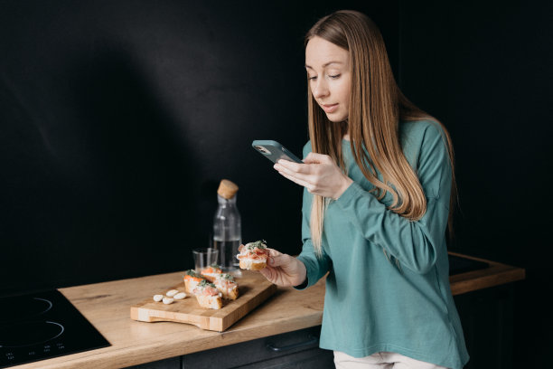 一个年轻漂亮的女人在写烹饪博客。关于健康食品的视频博客。有魅力的女人正在电话里说话和做饭。图片下载