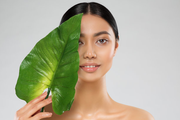 面部皮肤护理。美女模特盖脸大绿色热带树叶。亚洲女孩清新干净光滑的化妆超过白色。美少女水疗护理图片下载