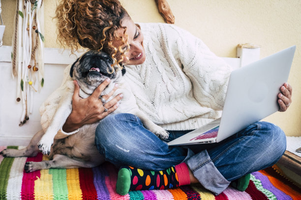 爱狗人士抱着她的小狗坐在长椅上，用无线连接的笔记本电脑上网。女性和她最好的朋友巴哥在网上玩得很开心，享受科技搜索图片下载