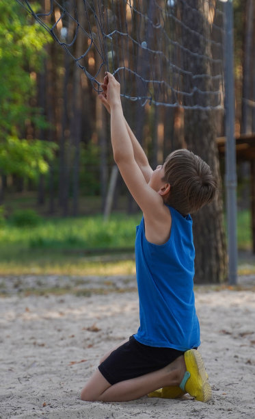青少年运动时尚。照片中，一个穿着运动服微笑着站在排球网旁的少年。图片下载