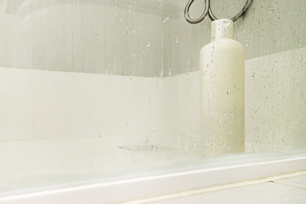 一个单独的洗发瓶放在一个玻璃封闭的淋浴间里，上面有水滴图片下载