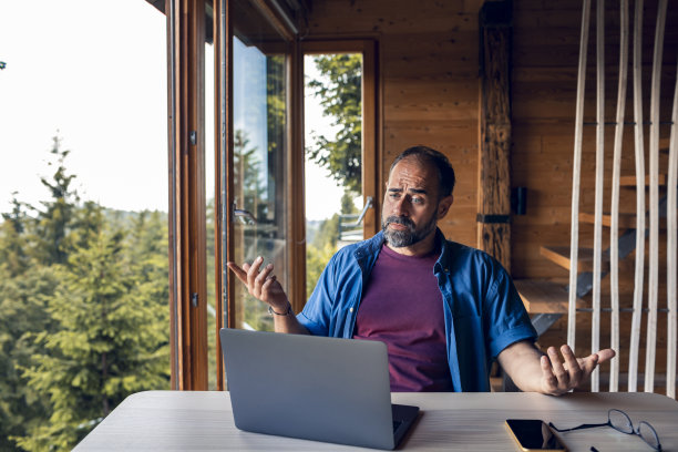 中年男子在俯瞰森林的小木屋里用笔记本电脑图片下载