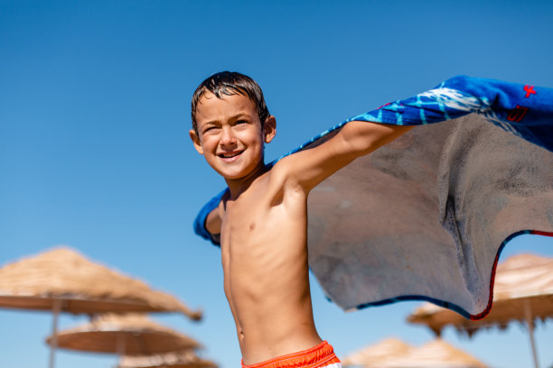 男孩在沙滩上用毛巾玩超级英雄图片下载