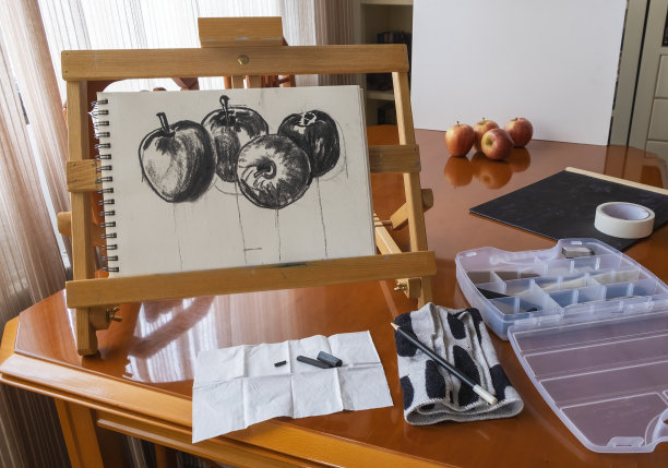 用木炭画水果，四个苹果，在便携式画架上的速写本上。图片下载