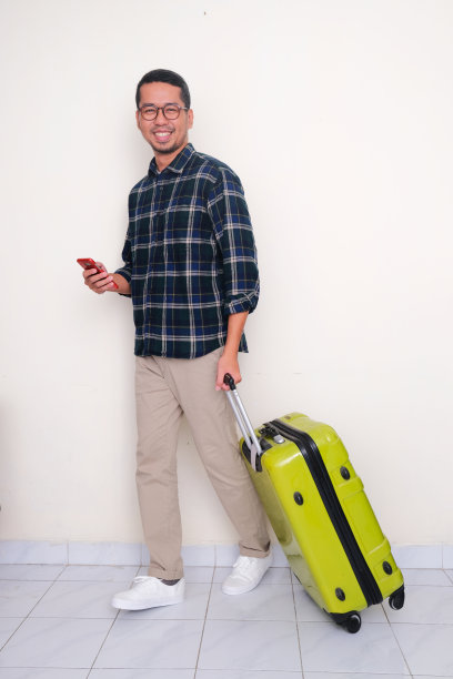 一名亚洲男子一边拉行李一边拿着手机走路的全身照片图片下载