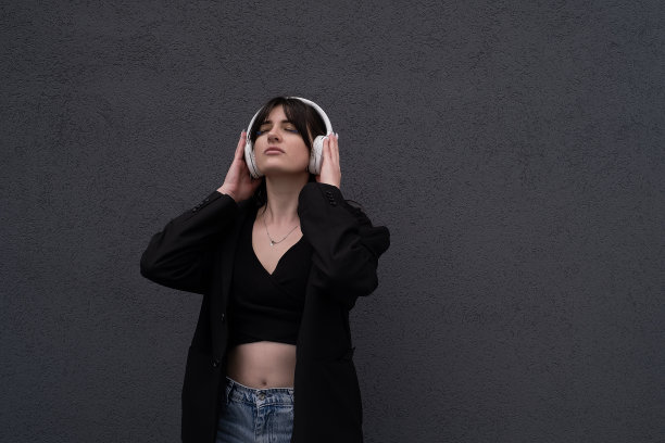 无忧无虑迷人的黑发女孩，穿着灰色毛衣，戴着耳机听音乐，站在灰色的背景上图片下载