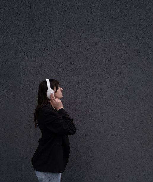 无忧无虑迷人的黑发女孩，穿着灰色毛衣，戴着耳机听音乐，站在灰色的背景上图片下载