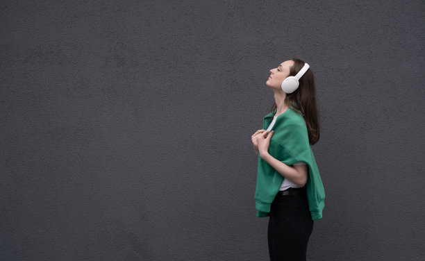 无忧无虑迷人的黑发女孩，穿着灰色毛衣，戴着耳机听音乐，站在灰色的背景上图片下载