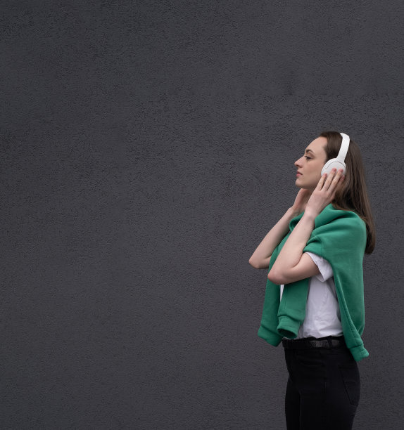 无忧无虑迷人的黑发女孩，穿着灰色毛衣，戴着耳机听音乐，站在灰色的背景上图片下载