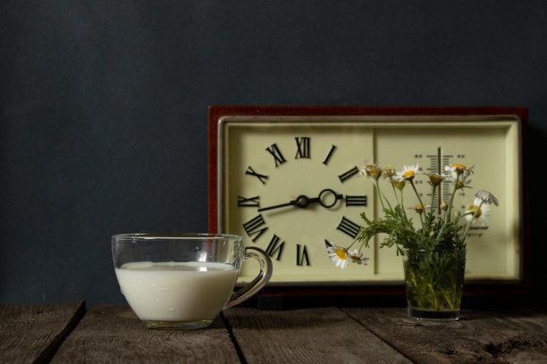 一杯牛奶和一个插着雏菊的花瓶，放在厨房木桌上的钟旁边图片下载