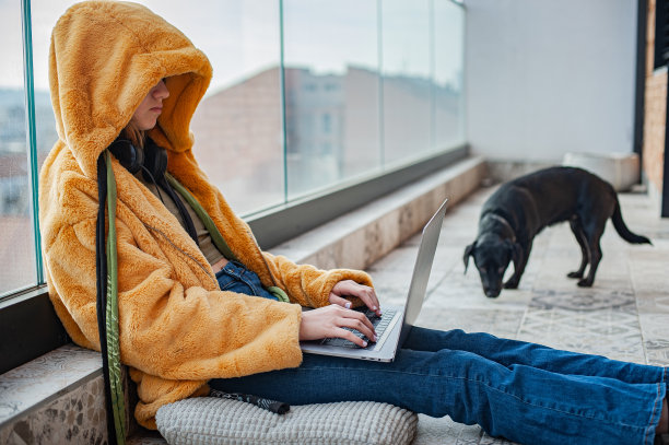 十几岁的女孩坐在阳台上用笔记本电脑，天空的背景图片下载