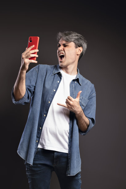 一名巴西男子的肖像，穿着纽扣衬衫和牛仔裤，用智能手机拍了一张表情丰富的自拍照，头发灰白——彩色照片——巴西图片下载