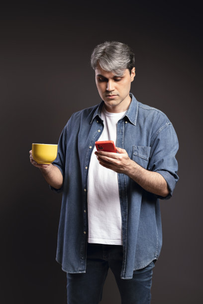 一个巴西男人的肖像，穿着衬衫和牛仔裤，拿着杯子，用他的智能手机，灰白的头发——彩色照片——巴西图片下载