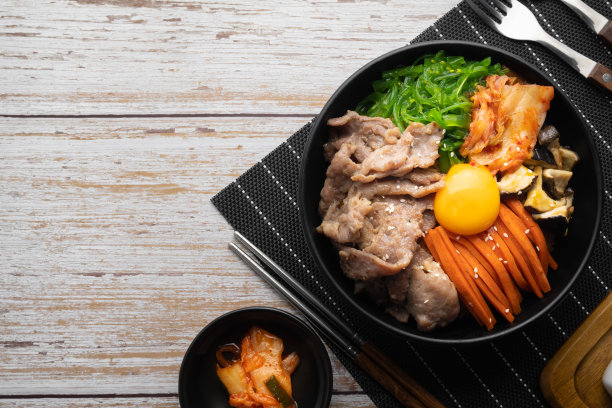 在木桌上用黑碗盛有牛腩、裙带菜和生鸡蛋的泡菜炒饭(拌饭)。图片下载