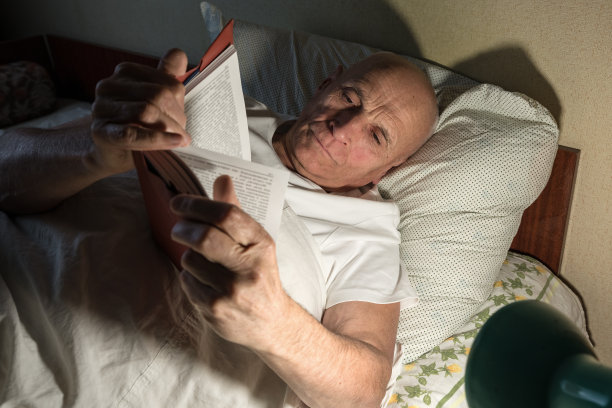 老人独自一人躺在床上，在电灯下看书图片下载