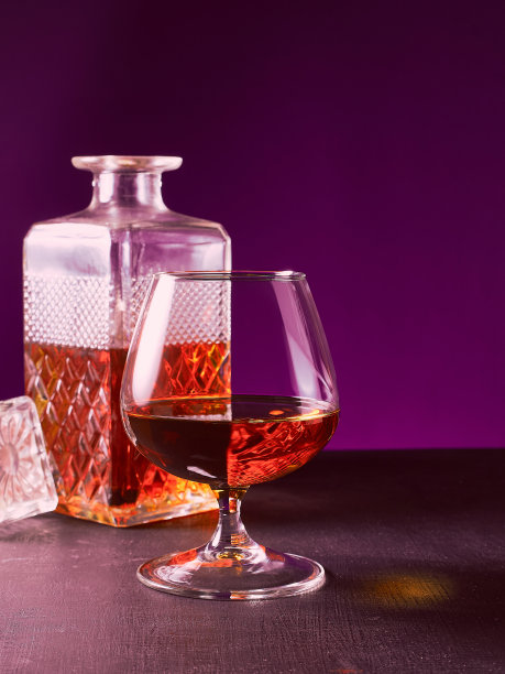 玻璃纹理方形瓶和玻璃高脚杯与琥珀酒精白兰地苏格兰威士忌。紫色的背景图片下载