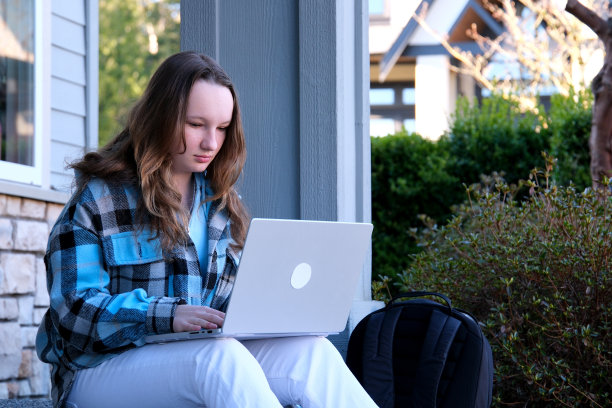 自信微笑的女人在户外工作，在笔记本电脑上打字。学生坐在街上用电脑做家庭作业。图片下载