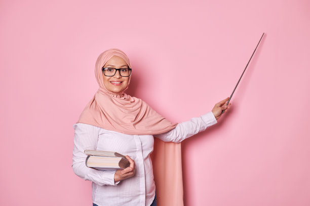 戴着粉红色头巾和眼镜的怀孕的穆斯林女教师，对着镜头微笑，指着复印处讲解课程图片下载
