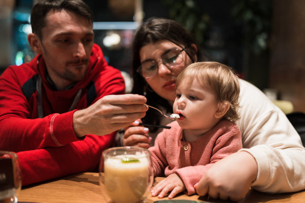 年轻的父母在咖啡馆给蹒跚学步的女儿喂冰淇淋。图片下载