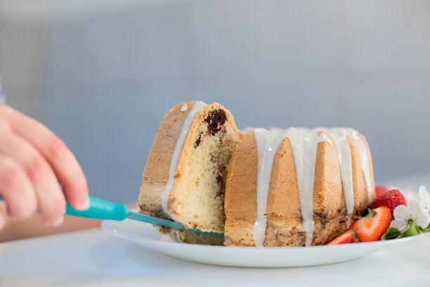 一名年轻女子正在切一款以春天为灵感的kugelhopf蛋糕，蛋糕上装饰着白花和草莓，她举起一块蛋糕给大家看图片下载