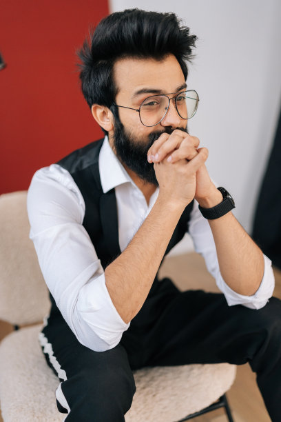 胡须绅士的垂直肖像，穿着优雅的正装，坐在椅子上，自信地望向别处。戴眼镜的印度年轻人的正面照片图片下载