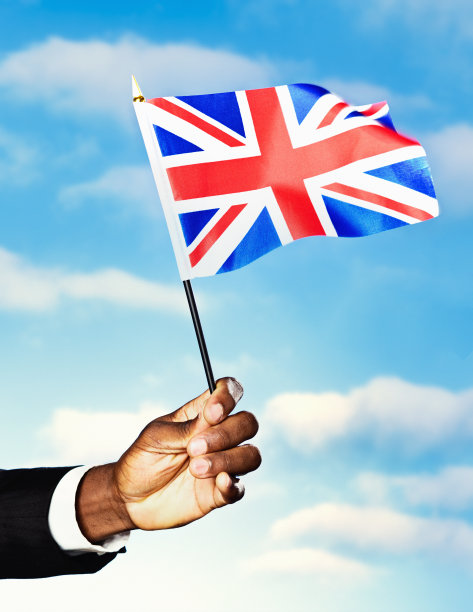 男性的手挥舞着英国国旗，天空中飘着蓬松的云图片下载