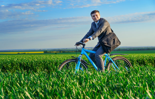 一位商人骑着自行车在绿油油的草地上，穿着商务套装，春日里美丽的大自然，自由职业者的经营理念图片下载