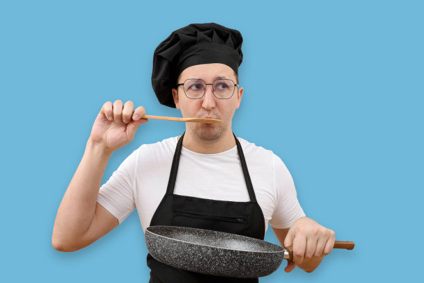 年轻的厨师在蓝色背景下用煎锅品尝食物。烹饪与人的概念图片下载