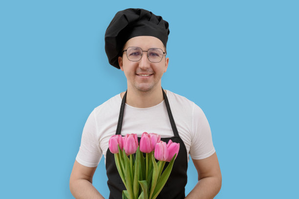 快乐的厨师拿着花看着蓝色背景的相机。烹饪与人的概念图片下载